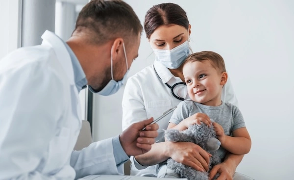 two doctors, one female and one male, gently engage with a young boy during a medical consultation