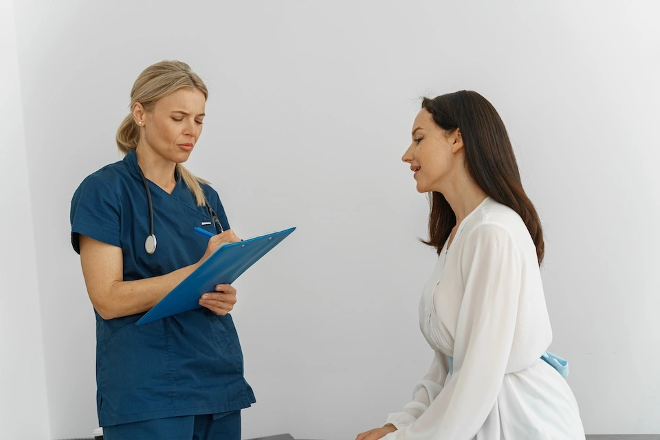 female doctor conducts a preventative health examination of a female patient sitting on a bed